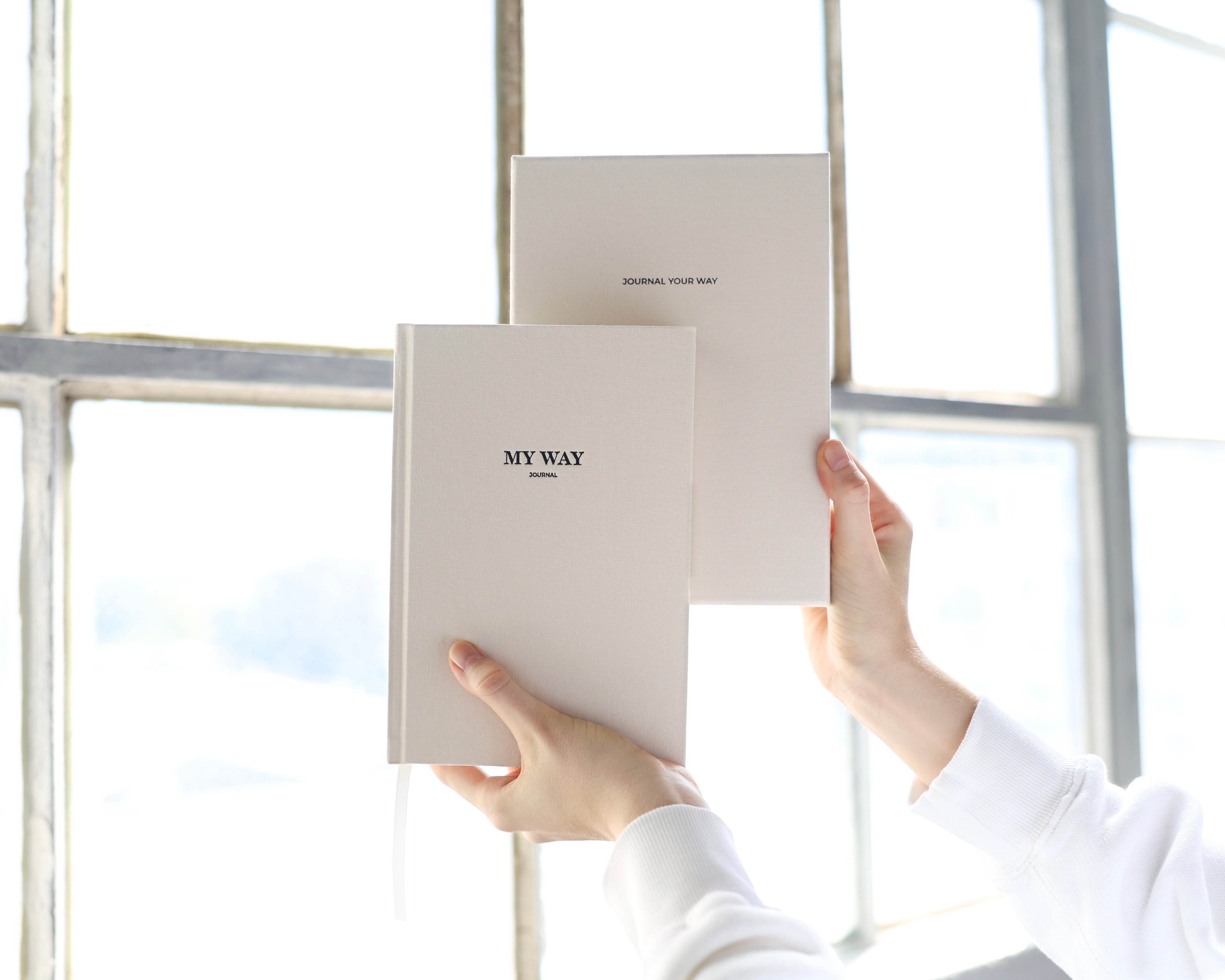 Hands holding the beige linen My Way Journal and matching gift box in front of a bright window, showcasing the premium materials of the My Way Journal undated planner and reflection journal.