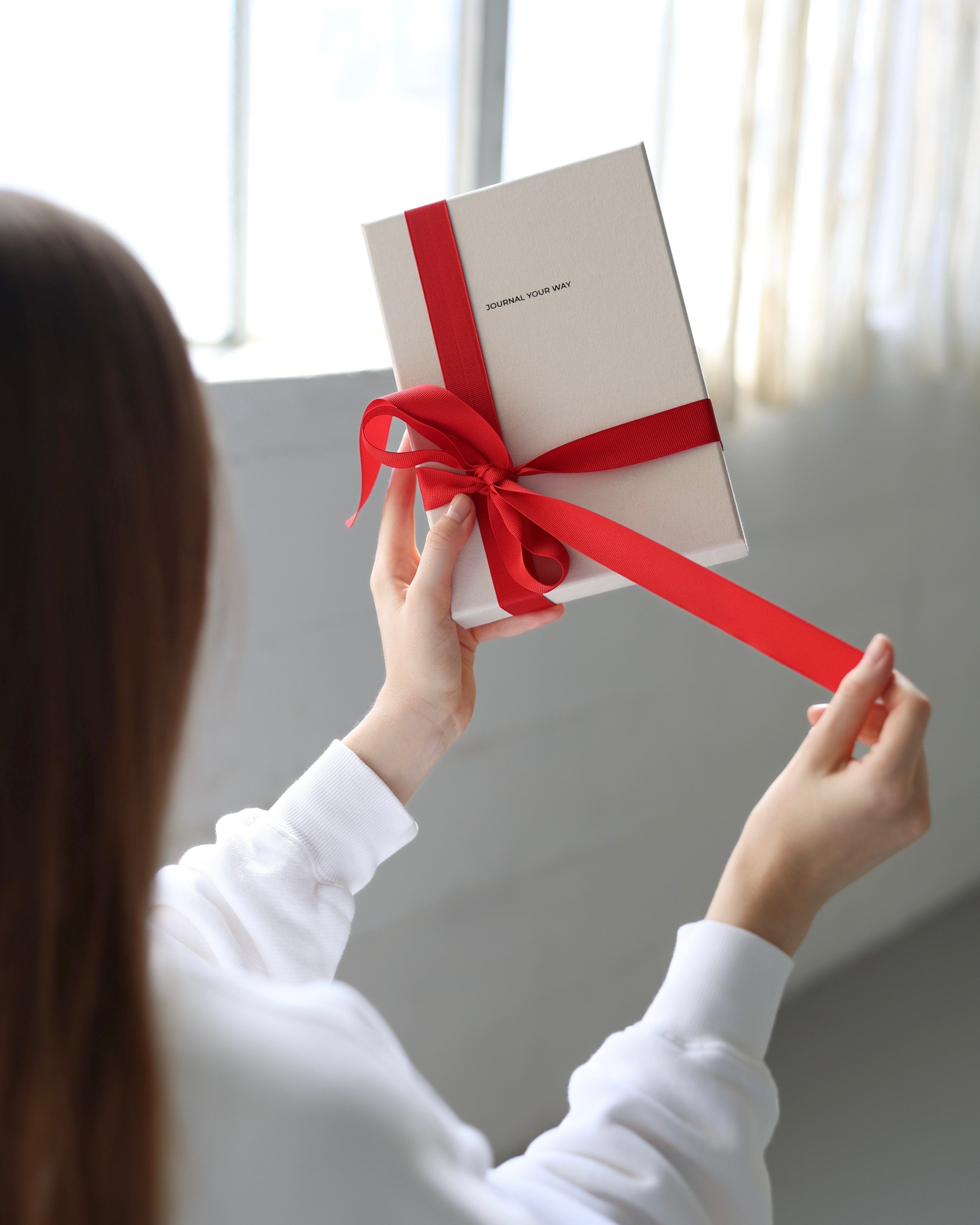 Person holding the My Way Journal gift box wrapped with a red ribbon in soft natural light, showing the journal’s premium linen packaging.
