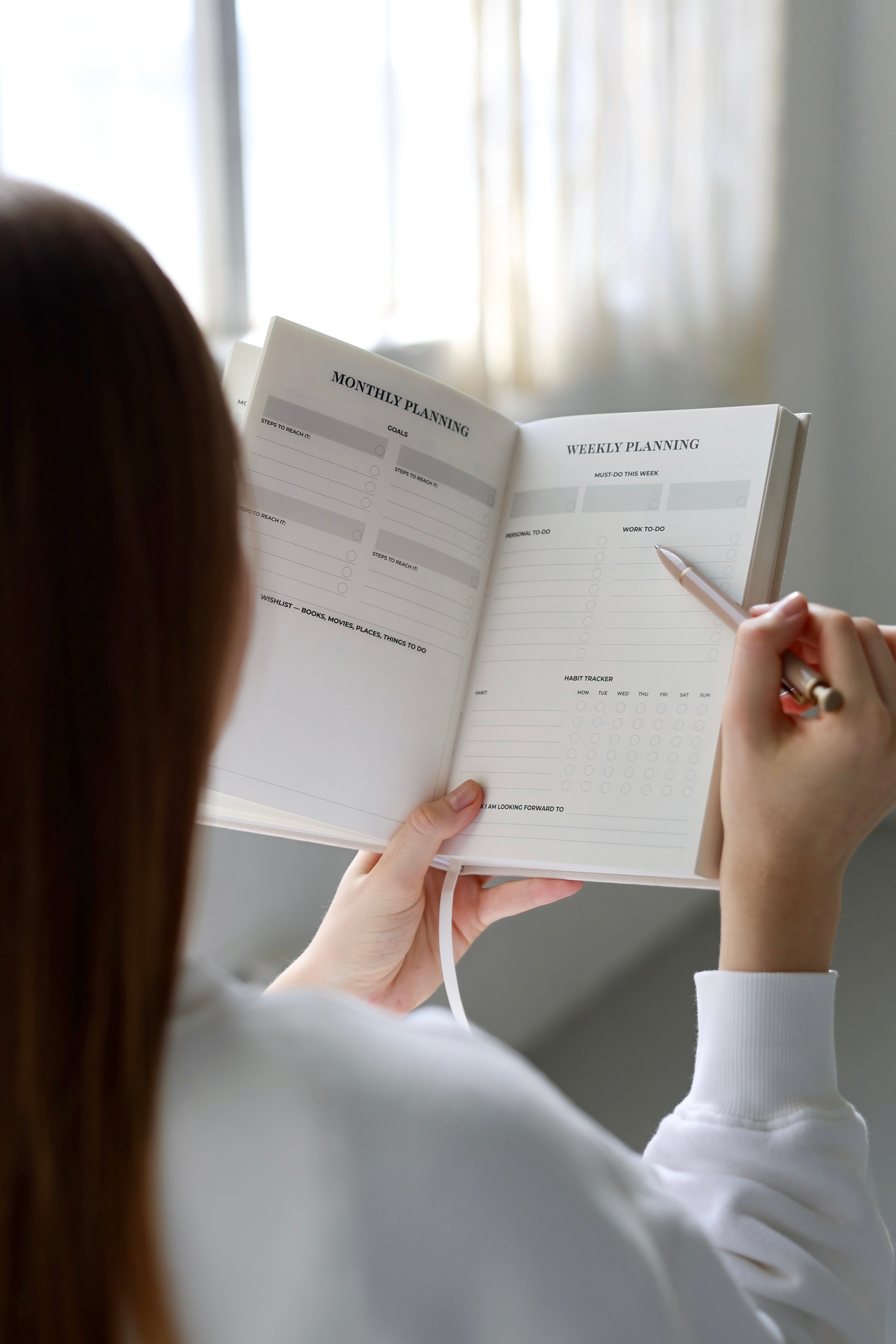 Person planning in the My Way Journal by a window, using an undated planner for mindful planning and reflection.